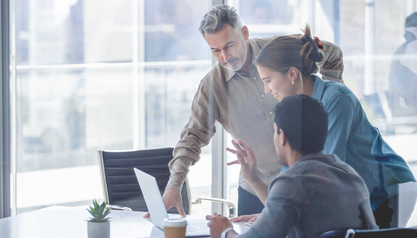 Drei Personen arbeiten in einem hellen Büro und tauschen sich angeregt aus.