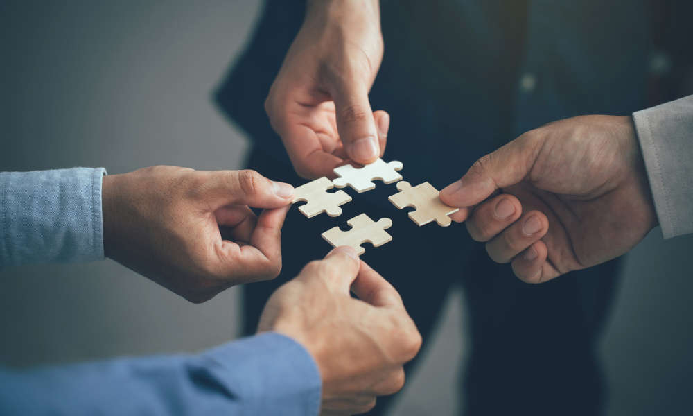 Stimmungsbild: Vier Personen symbolisieren Teamwork, indem sie vier passende Puzzlestücke zu einem Ganzen zusammensetzen.