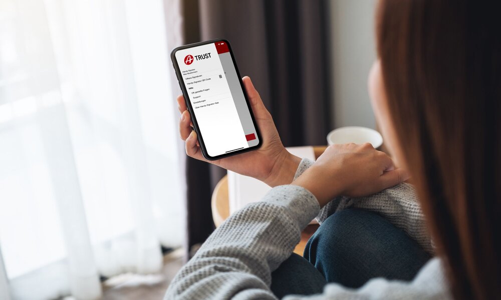 Stimmungsbild: Blick über die Schultern einer Frau auf ein Smartphone mit geöffneter A-Trust Signatur App.