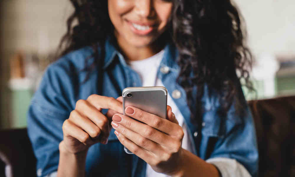 Stimmungsbild: Frau nutzt ihr Smartphone und lächelt dabei.