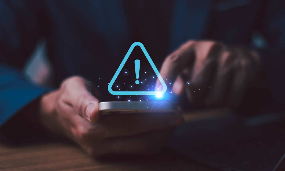Montage: Person hält ein Smartphone in dunkler Umgebung. Über dem Display schwebt ein leuchtendes blaues Warndreieck-Icon mit Ausrufezeichen.