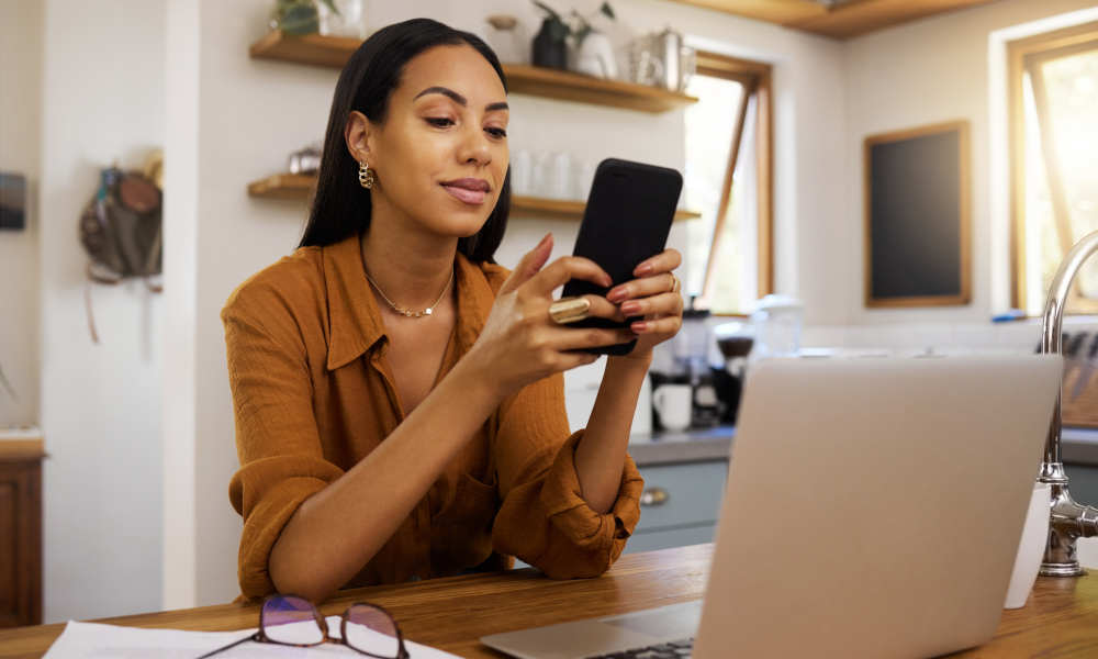 Imagebild: Frau im Homeoffice sitzt vor ihrem Laptop und nutzt ihr Smartphone