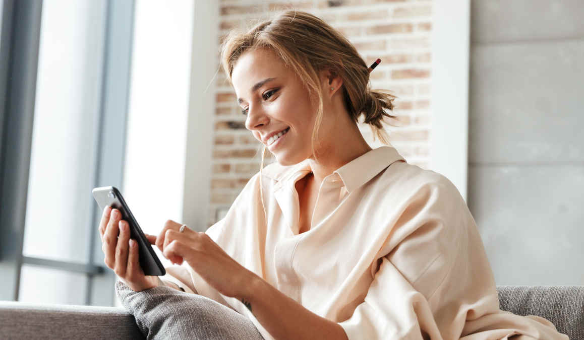 Stimmungsbild: Eine junge Frau sitzt lässig auf der Couch und nutzt ihr Smartphone.