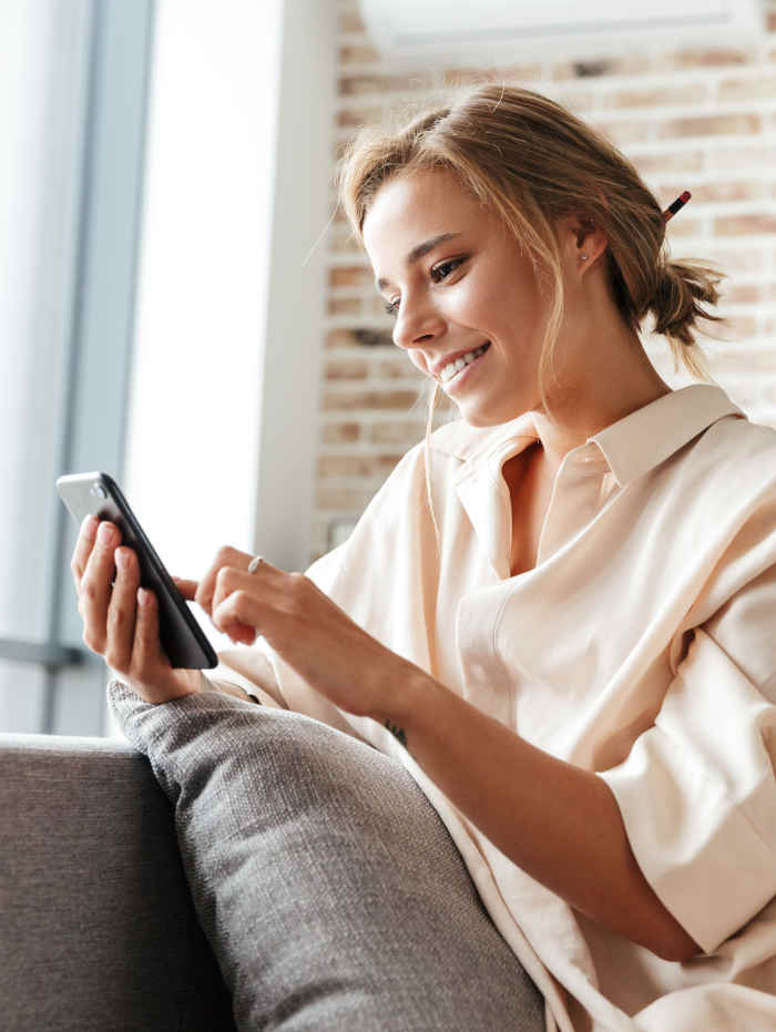 Stimmungsbild: Eine junge Frau sitzt lässig auf der Couch und nutzt ihr Smartphone.