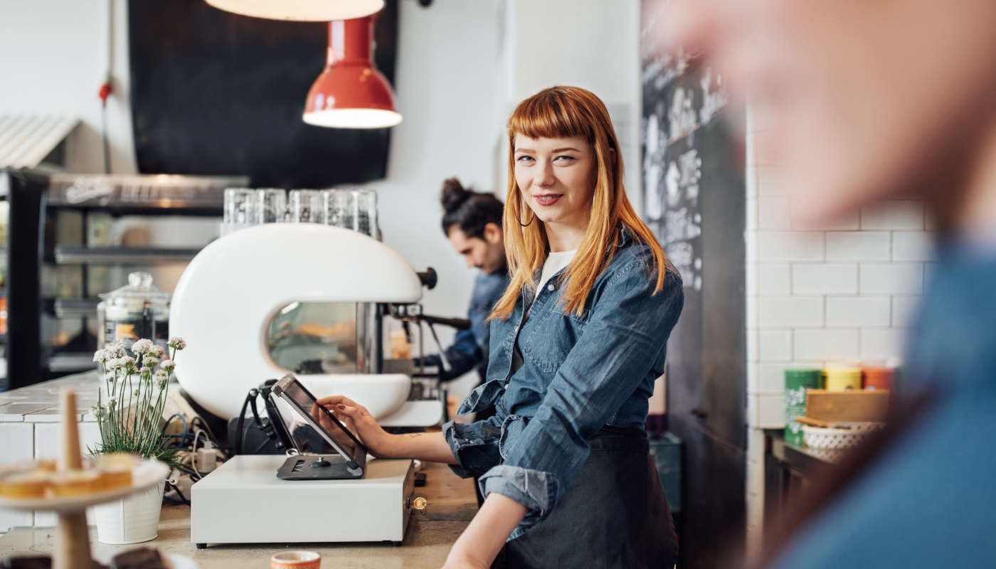 Sympathische junge Frau bedient eine Registrierkasse im Café.