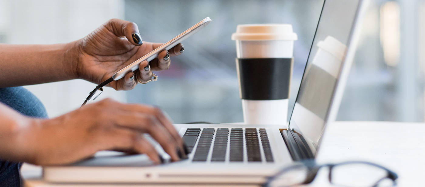 Eine Frau arbeitet am Laptop und hält in der linken Hand ein Smartphone.