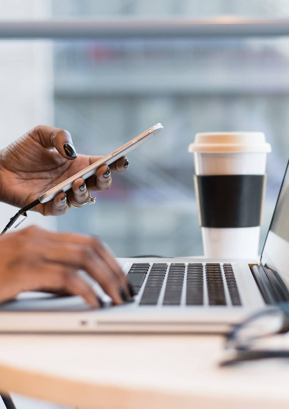 Eine Frau arbeitet am Laptop und hält in der linken Hand ein Smartphone.